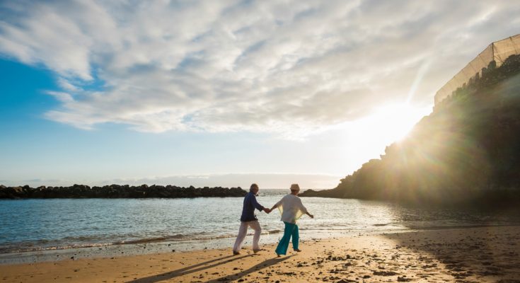 retired couple walking on a beach at sunset